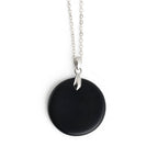 Black circular pendant on a silver chain against a white background